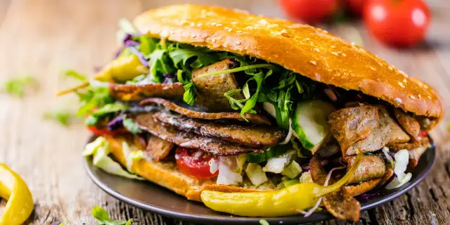 Kebab w bułce z mięsem, warzywami i sosem na drewnianym tle.