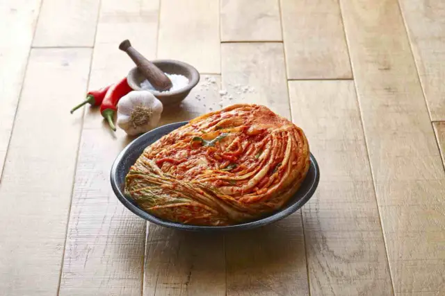 Cała główka kapusty pekińskiej w misce, obok papryczki chili, czosnek i moździerz z solą.