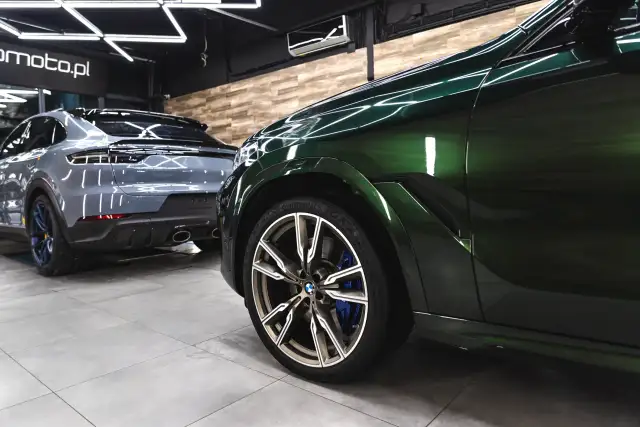 Błyszczące, zielone BMW i szary Porsche w profesjonalnym studiu auto detailing.