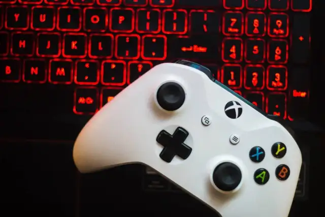 Biały kontroler Xbox One na tle podświetlanej na czerwono klawiatury.