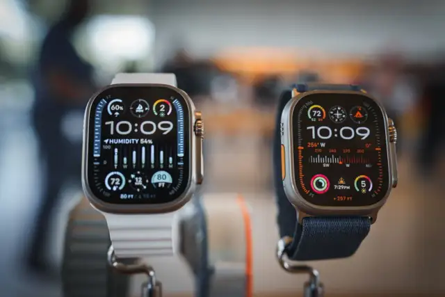 Deux montres connectées Apple, l'une avec bracelet blanc, l'autre bleu, affichent l'heure et des données météo.