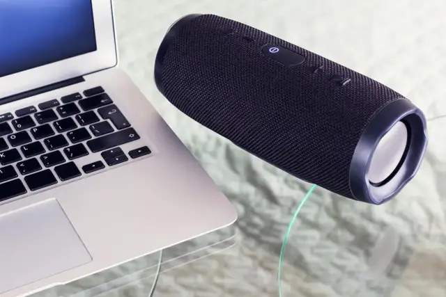 Un ordinateur portable et une enceinte Bluetooth noire sur une table en verre. Apprenez comment connecter une enceinte Bluetooth pour une expérience audio sans fil.