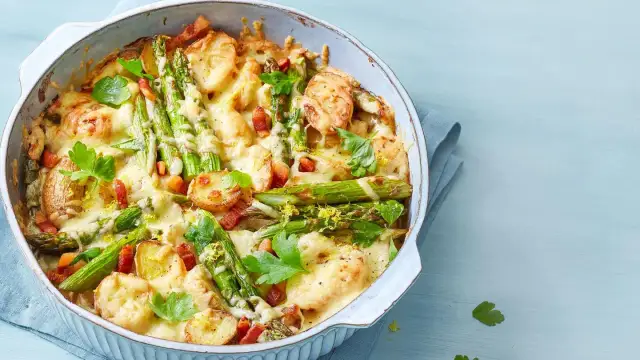Herzhafter Spargel Auflauf mit Kartoffeln, Speck und geschmolzenem Käse, garniert mit Petersilie und Zitronenschale.