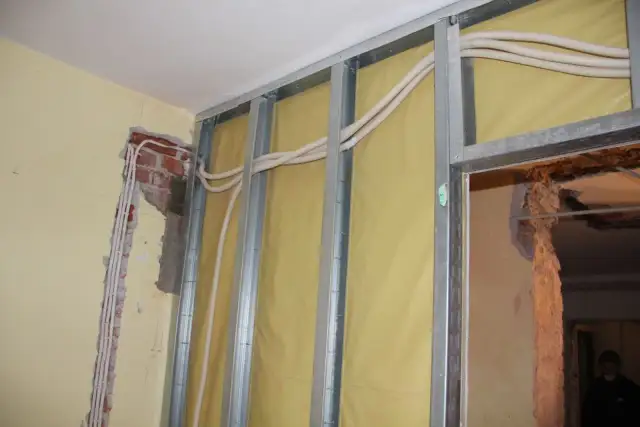 Nowa instalacja elektryczna bez kucia ścian. Widoczne profile metalowe, izolacja i nowe przewody w peszlach.