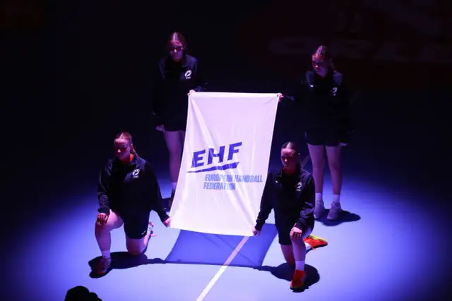 Cztery młode kobiety prezentują flagę EHF przed meczem ligi mistrzów w piłce ręcznej mężczyzn.