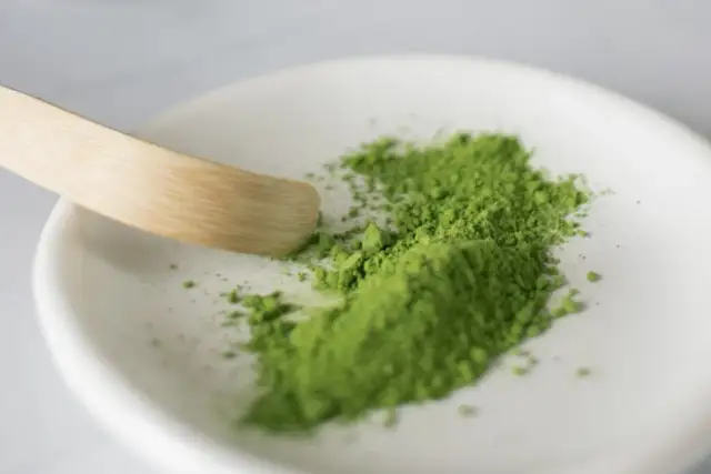 Zielony proszek matcha na białej miseczce z bambusową łopatką.