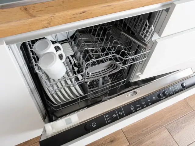 Wnętrze zmywarki Whirlpool 6th Sense z koszami pełnymi naczyń, w tym kubków i talerzy.
