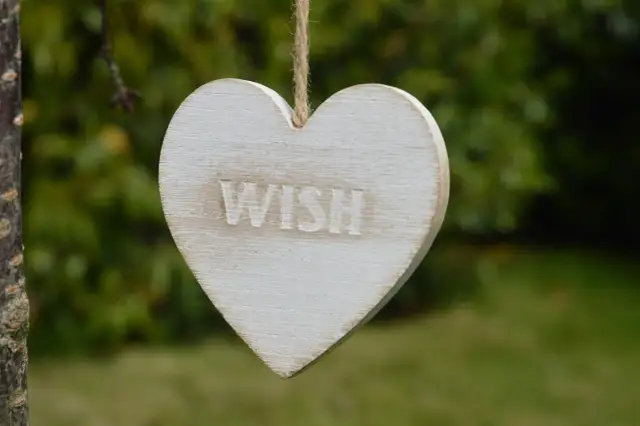 Drewniane serce z napisem "WISH" wisi na sznurku. Idealne na życzenia urodzinowe dla podróżnika, by spełniły się jego marzenia o dalekich wyprawach.