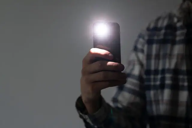 Dłoń trzyma smartfon z włączoną latarką.