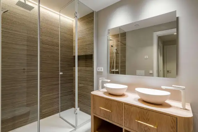 Baños pequeños con encanto: ducha con paredes de madera acanalada y tocador de madera con dos lavabos blancos.