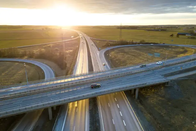 Widok z lotu ptaka na węzeł autostradowy o zachodzie słońca, z samochodami na jezdni.