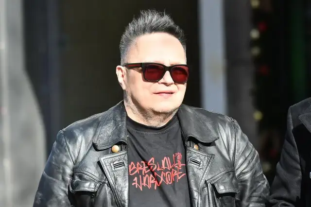Charyzmatyczny wokalista w skórzanej kurtce i okularach przeciwsłonecznych, z charakterystyczną fryzurą.