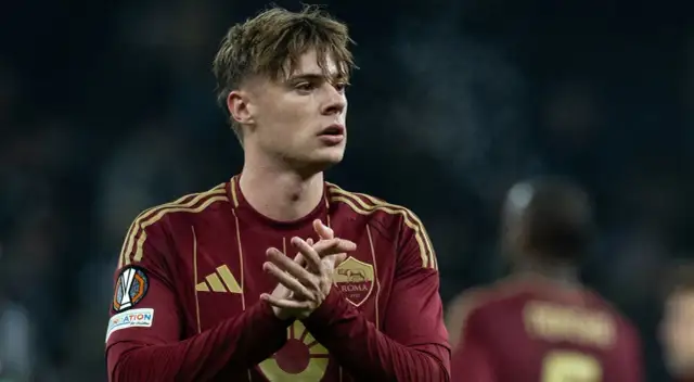 Piłkarz Nicola Zalewski w bordowej koszulce AS Roma z żółtymi pasami na ramionach.
