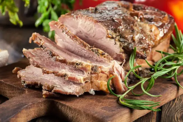 Pokrojony, pieczony boczek z ziołami na desce. Idealny przykład, jak zapeklować boczek do pieczenia, by był soczysty i aromatyczny.