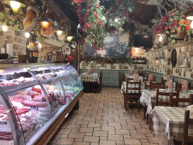 Wnętrze restauracji w stylu rustykalnym, z wiszącymi wędlinami i dekoracjami. W chłodni mnóstwo wyrobów, jak w najlepszym sklepie w Frascati.