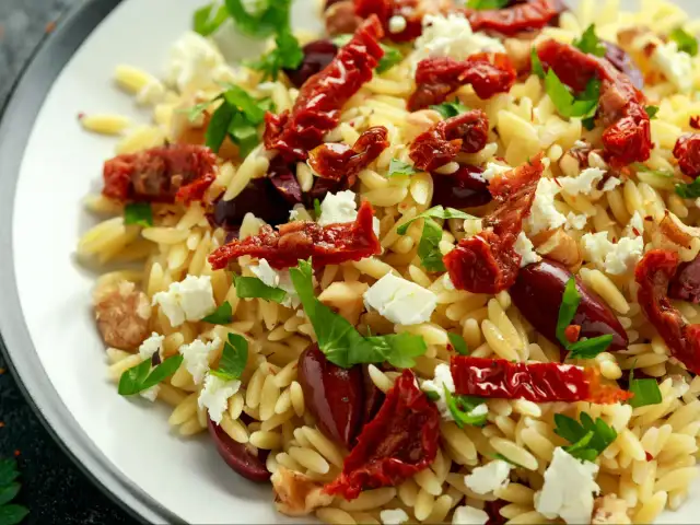 Pyszna sałatka z makaronu orzo, suszonych pomidorów, oliwek, sera feta i świeżej bazylii.