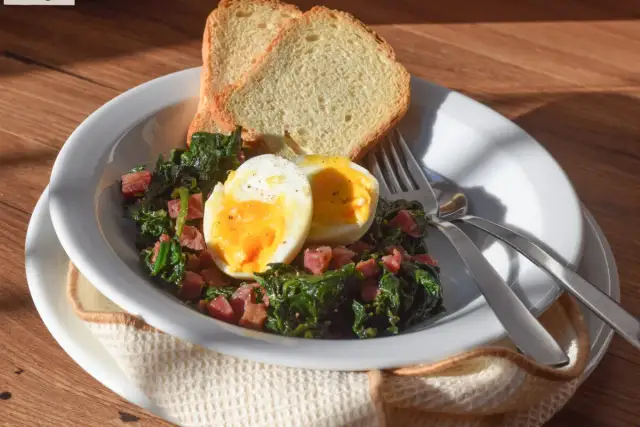 Plato de espinacas con jamón, huevo duro y tostadas. Un desayuno o almuerzo saludable y delicioso.
