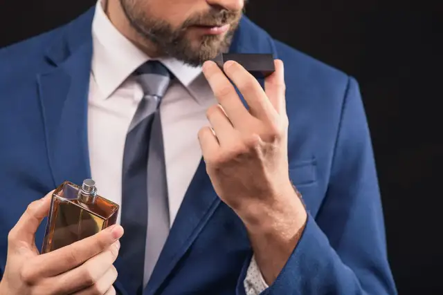 Mężczyzna w garniturze wącha perfumy z buteleczki.