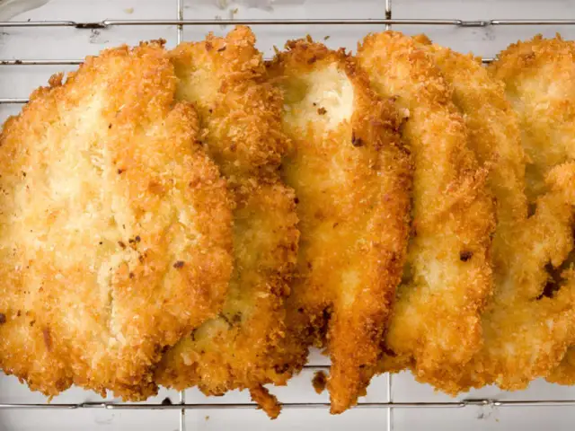 Fileteadas pechugas de pollo empanadas, doradas y crujientes, reposan sobre una rejilla metálica.