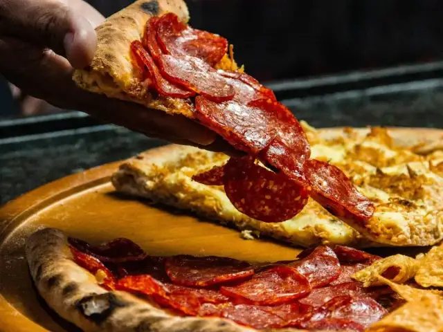 Kawałek pizzy pepperoni unoszony nad całą pizzą na drewnianej desce.