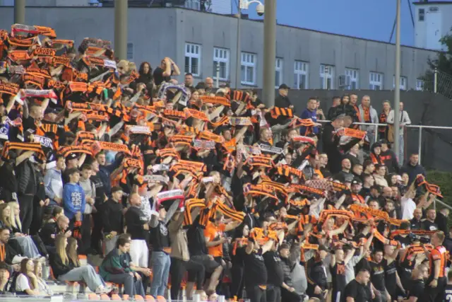 Tłum kibiców na stadionie z szalikami w barwach pomarańczowo-czarnych. Widać napisy "Chrobry" i "Chrobry Głogów".