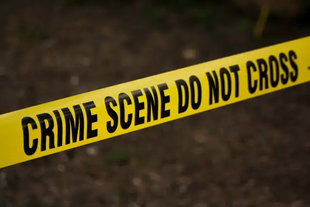 Żółta taśma z napisem "CRIME SCENE DO NOT CROSS" na ciemnym tle.