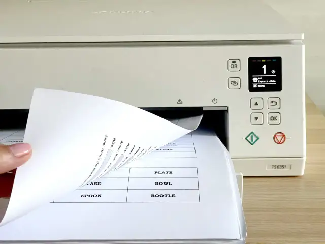 Dłoń wsuwa papier do drukarki, na ekranie widoczny numer 1 i opcja "Kopia cz.-biała".