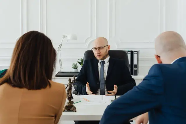 Prawnik wyjaśnia parze, jak napisać wniosek o rozwód. Na stole widać figurkę Temidy.