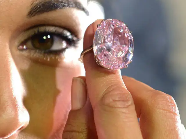 Ein riesiger, pinker Diamantring wird von einer Hand gehalten. Man fragt sich, wie viel kostet ein Kilo Diamant?