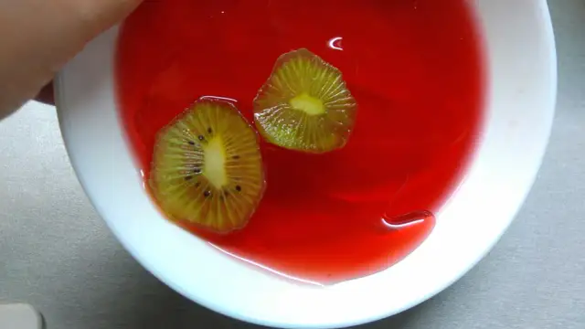 Dwa plastry kiwi w czerwonej galaretce w białej misce.
