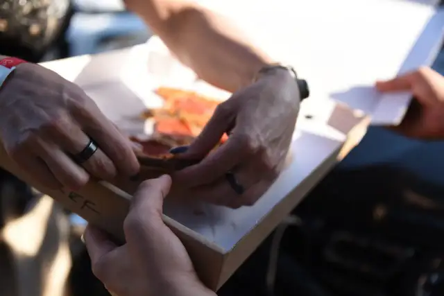 Dwie osoby dzielą się pizzą z pudełka. Właśnie pokazują sobie, jak jeść pizzę, by każdy dostał swój kawałek.