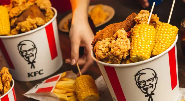 Wiadro KFC z kurczakiem, frytkami i kolbami kukurydzy.