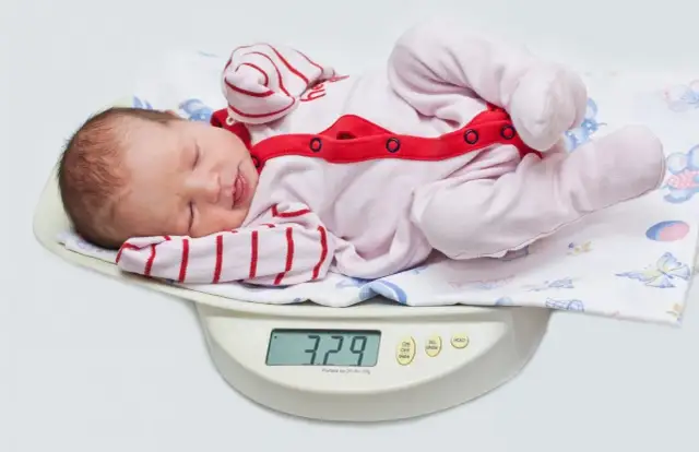 Nowe życie waży 3,29 kg. Dziecko po urodzeniu leży na wadze, ubrane w różowy pajacyk w paski.