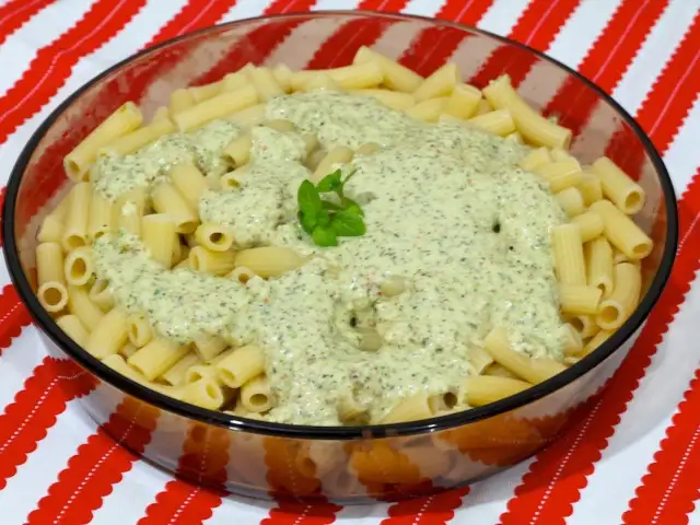 Macarrones al pesto servidos en un bol de cristal, con una hoja de albahaca fresca decorando la cremosa salsa verde.