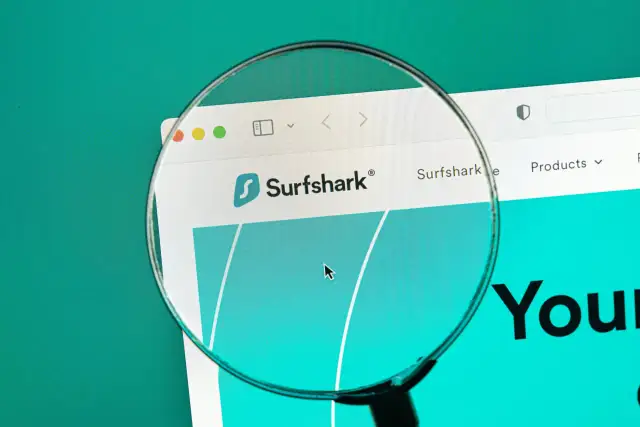 Lupa w telefonie powiększa logo Surfshark i fragment strony internetowej.