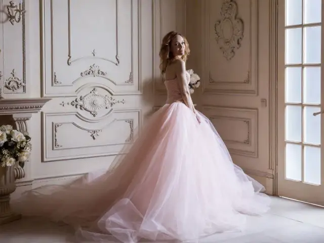 Kobieta w różowej sukni księżniczki z bukietem kwiatów w eleganckim wnętrzu.