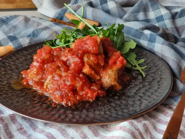 Magro con tomate, un plato casero con trozos de carne tierna bañados en una salsa de tomate casera, acompañado de rúcula fresca.