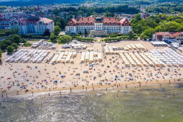 Plaża z leżakami i parasolami, w tle hotel Grand. Zastanawiasz się, ile kosztuje nocleg nad morzem w takim miejscu?