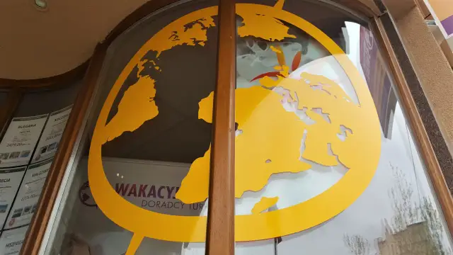Żółta mapa świata na szybie biura podróży z widocznymi ofertami wakacyjnymi.