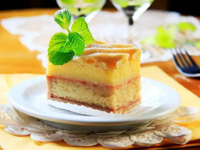 Kawałek tortu z warstwami ciasta, kremu i dżemu, ozdobiony miętą.