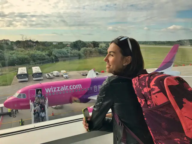 Kobieta z plecakiem patrzy na samolot Wizzair. Chcesz wiedzieć, jak zadzwonić do Wizzair za darmo? Sprawdź na stronie przewoźnika.