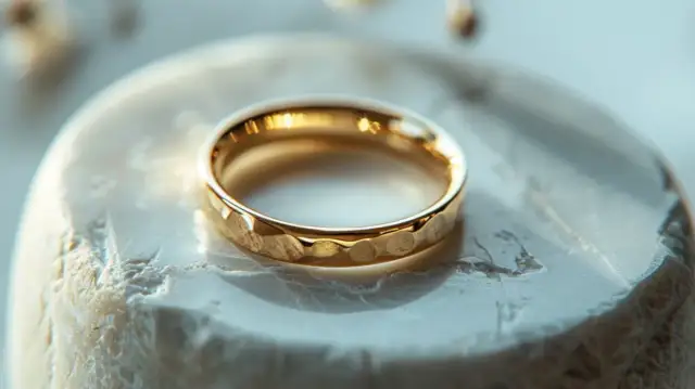 Złoty pierścionek z młotkowaną fakturą na białej, chropowatej powierzchni.