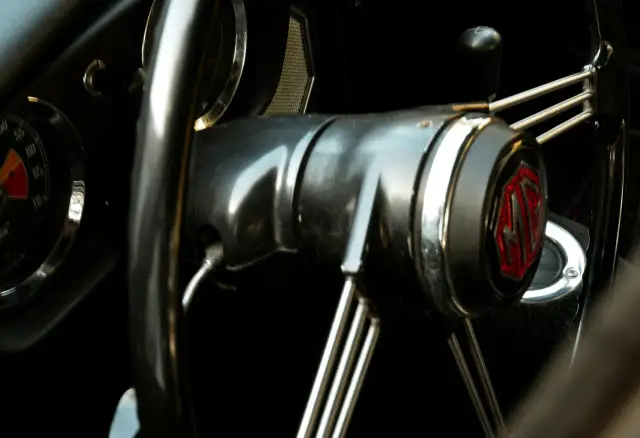 Wnętrze klasycznego MG. Kierownica z chromowanymi szprychami i emblematem MG. Słychać metaliczny pisk przy skręcaniu.