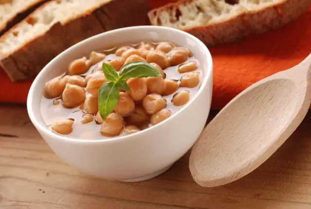 Miseczka ciecierzycy z bazylią, obok kromki chleba i drewniana łyżka.