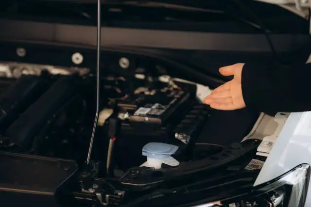 Oto zbiorniczek, gdzie wlać płyn do sprzęgła. Dłoń wskazuje na miejsce pod maską.