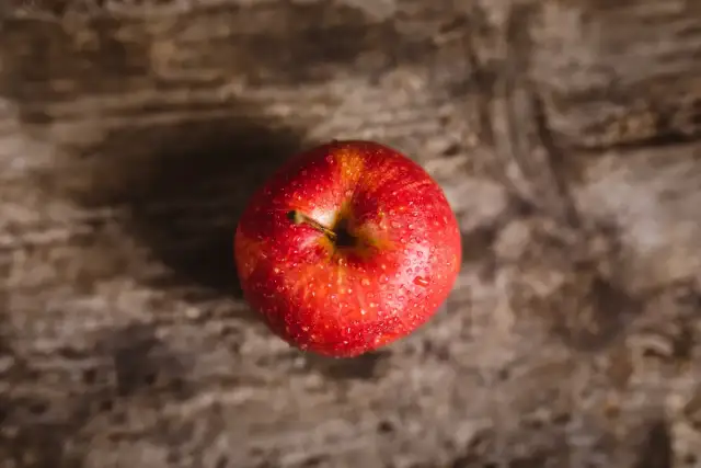 Czerwone jabłko z kroplami wody na drewnianym tle.