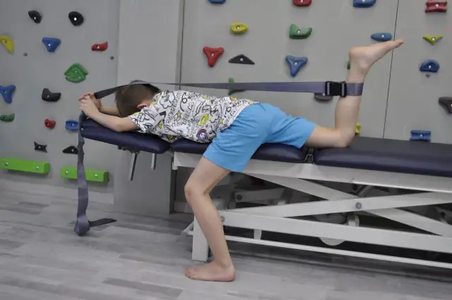 Chłopiec leży na kozetce, wykonując ćwiczenia na mięsień prosty uda z użyciem taśmy.