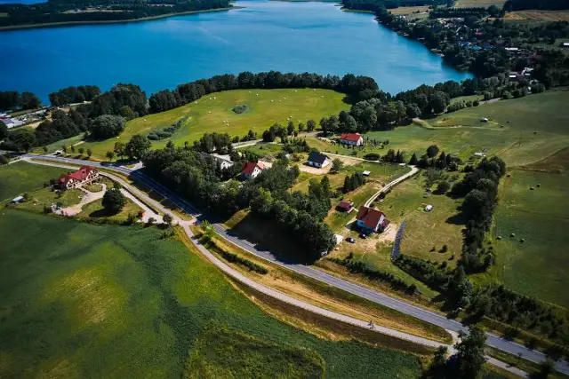 Malownicze **trasy rowerowe Mazury** wiodą przez zielone pola i lasy, w pobliżu błękitnego jeziora.