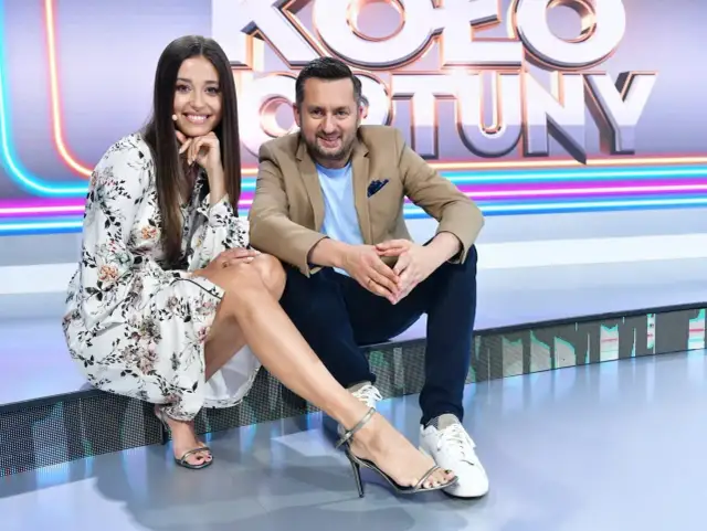 Uśmiechnięta para na planie "Koło Fortuny kto ubiera". Ona w kwiecistej sukience i sandałkach, on w marynarce i jeansach.