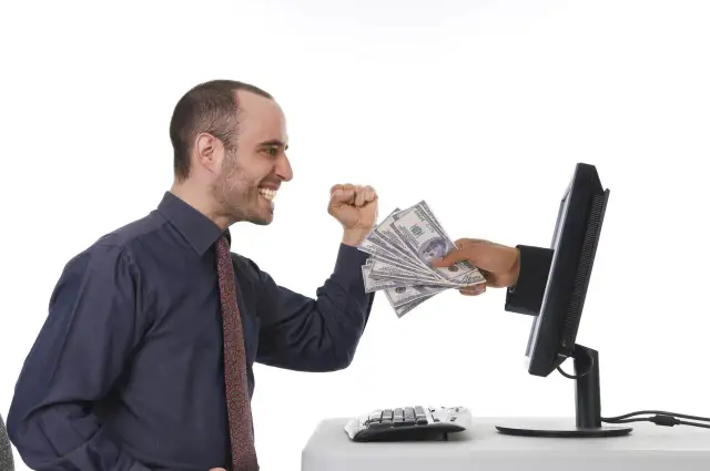Uśmiechnięty mężczyzna otrzymuje stos banknotów z ekranu komputera. To symbol zarabiania na klikaniu.